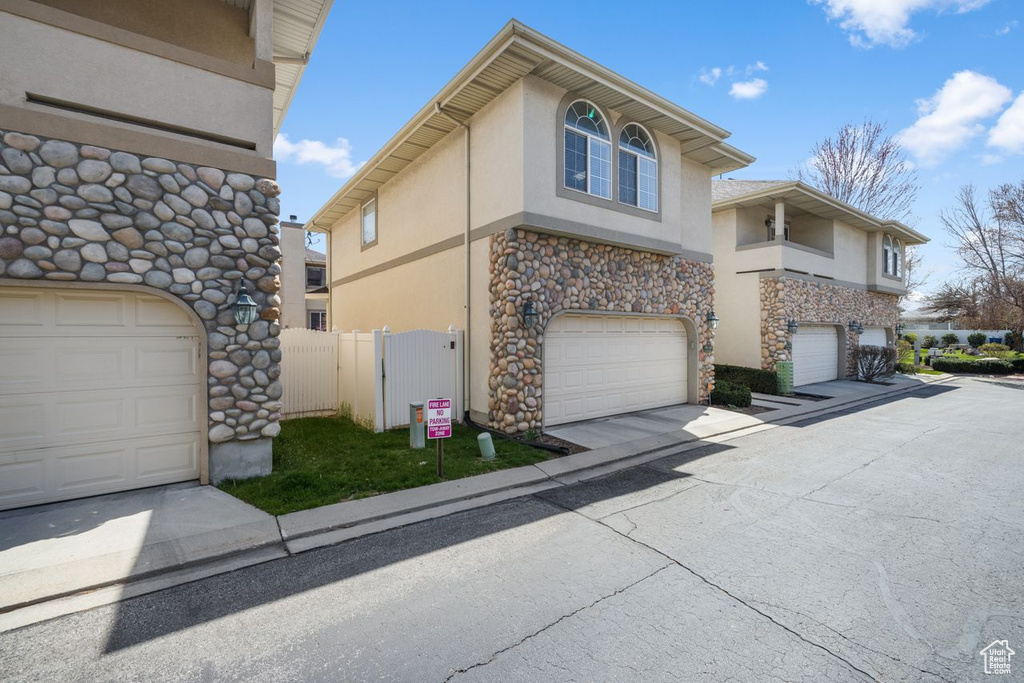 View of property exterior featuring an attached garage, stone siding, fence, stucco siding, and a gate
