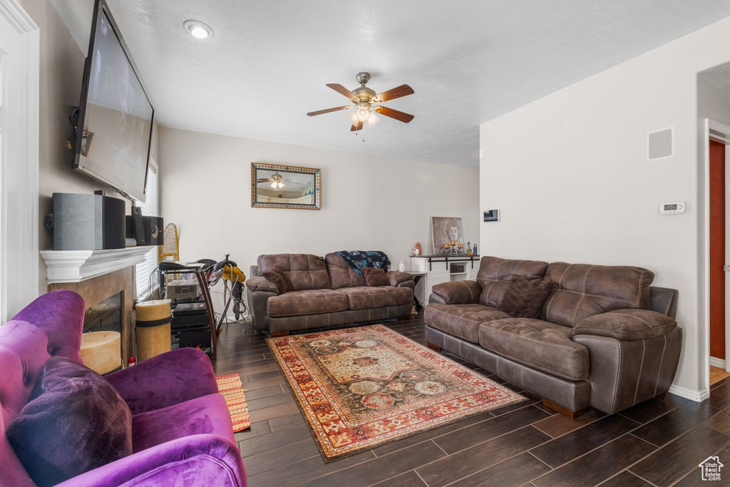 Living area featuring dark wood-type flooring, a tiled fireplace, a ceiling fan, and visible vents