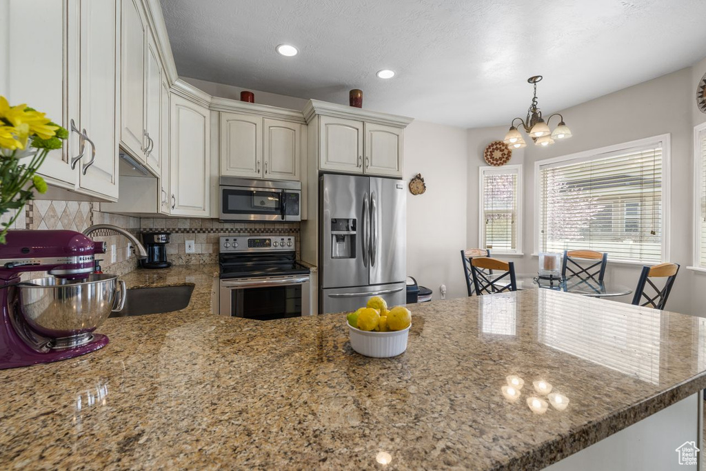 Kitchen featuring a notable chandelier, a sink, appliances with stainless steel finishes, a peninsula, and backsplash