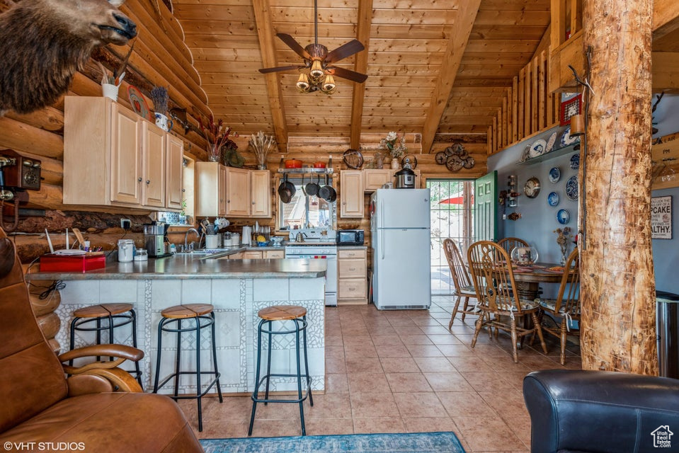 Kitchen featuring freestanding refrigerator, wooden ceiling with exposed beams, log walls, a sink, and black microwave
