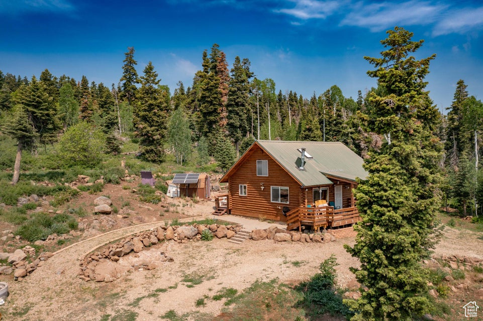View of side of home with an exterior structure, a deck, an outdoor structure, log siding, and a view of trees