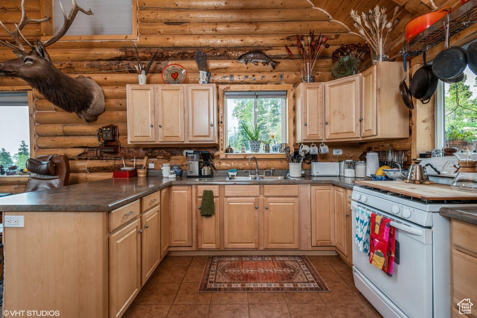 Kitchen featuring white range oven, log walls, a sink, and light brown cabinetry