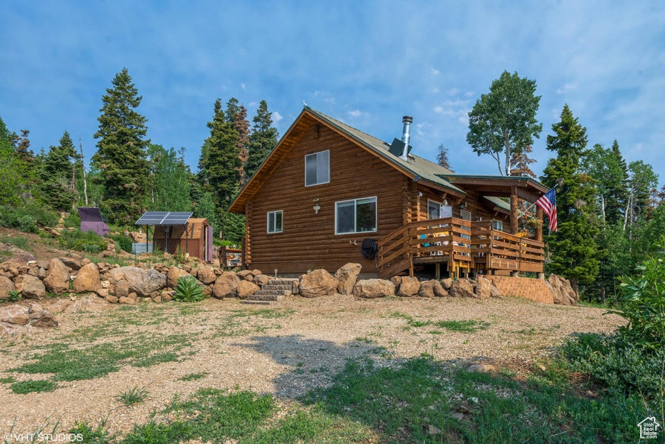 Back of property featuring log siding, an outbuilding, a deck, and a greenhouse