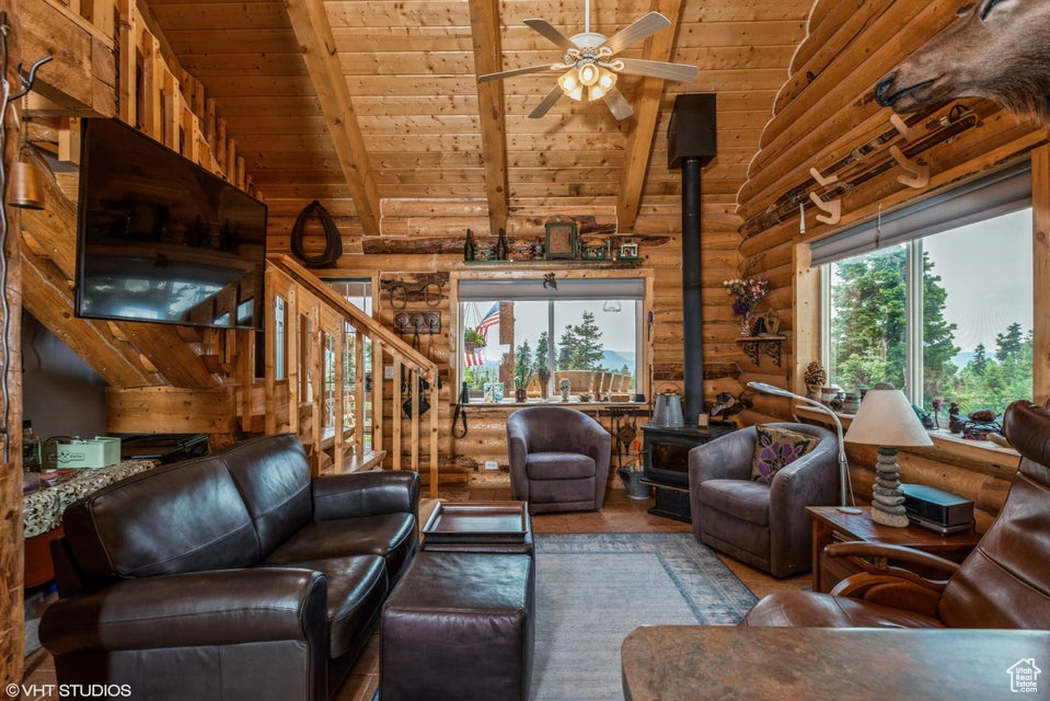 Living room with a wood stove, wood ceiling, rustic walls, ceiling fan, and wood finished floors