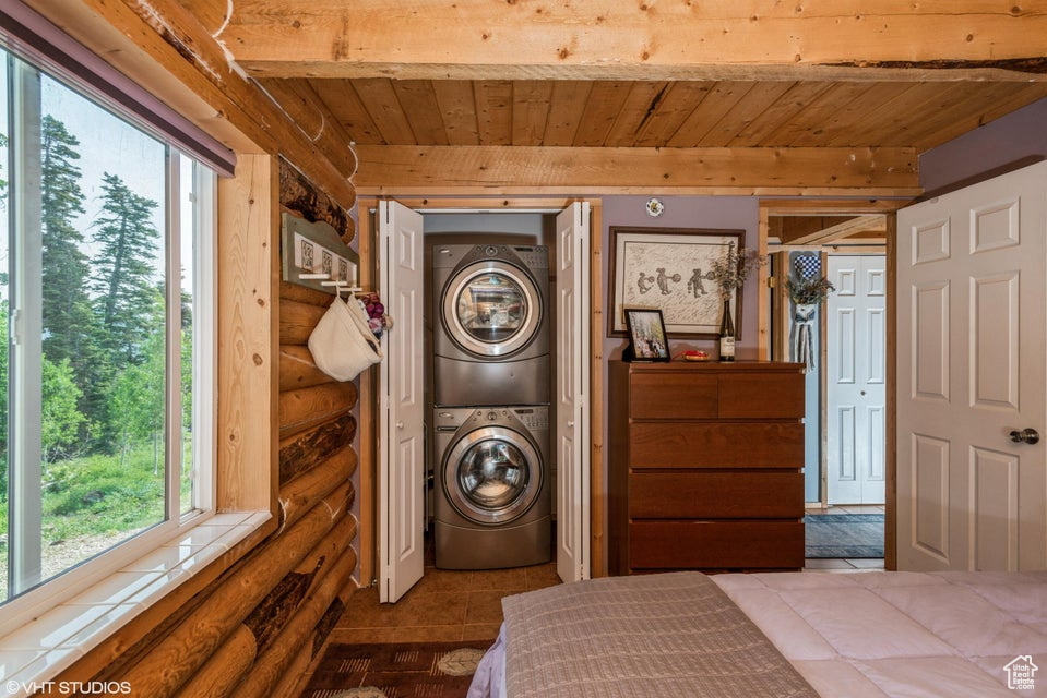 Bedroom with stacked washing machine and dryer, rustic walls, and wood ceiling with exposed beams