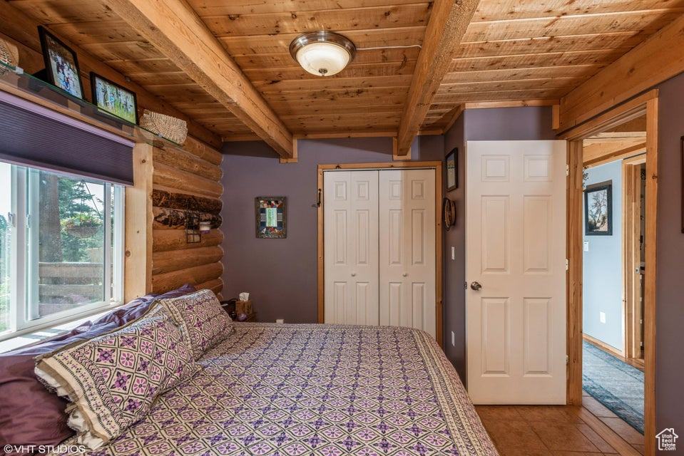 Bedroom with log walls, wood ceiling with exposed beams, a closet, and tile patterned floors