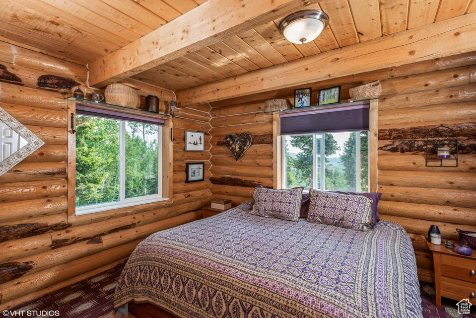 Bedroom featuring multiple windows, wood ceiling with exposed beams, and log walls