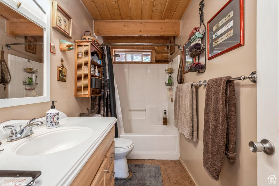 Full bathroom featuring wood ceiling, vanity, toilet, shower / bath combo with shower curtain, and tile patterned flooring