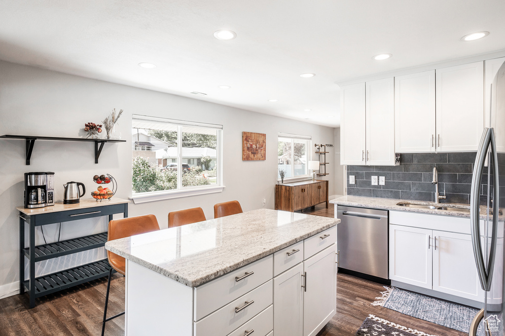Kitchen featuring stainless steel appliances, a sink, dark wood finished floors, a kitchen island, and white cabinetry