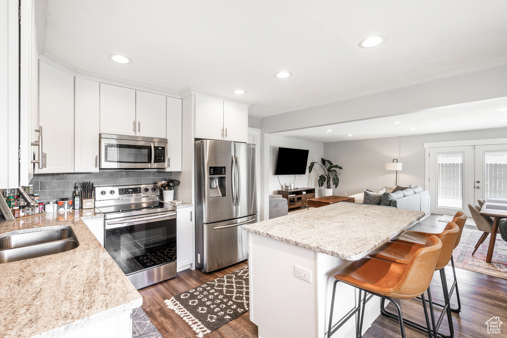 Kitchen featuring stainless steel appliances, a center island, dark wood-type flooring, white cabinetry, and open floor plan
