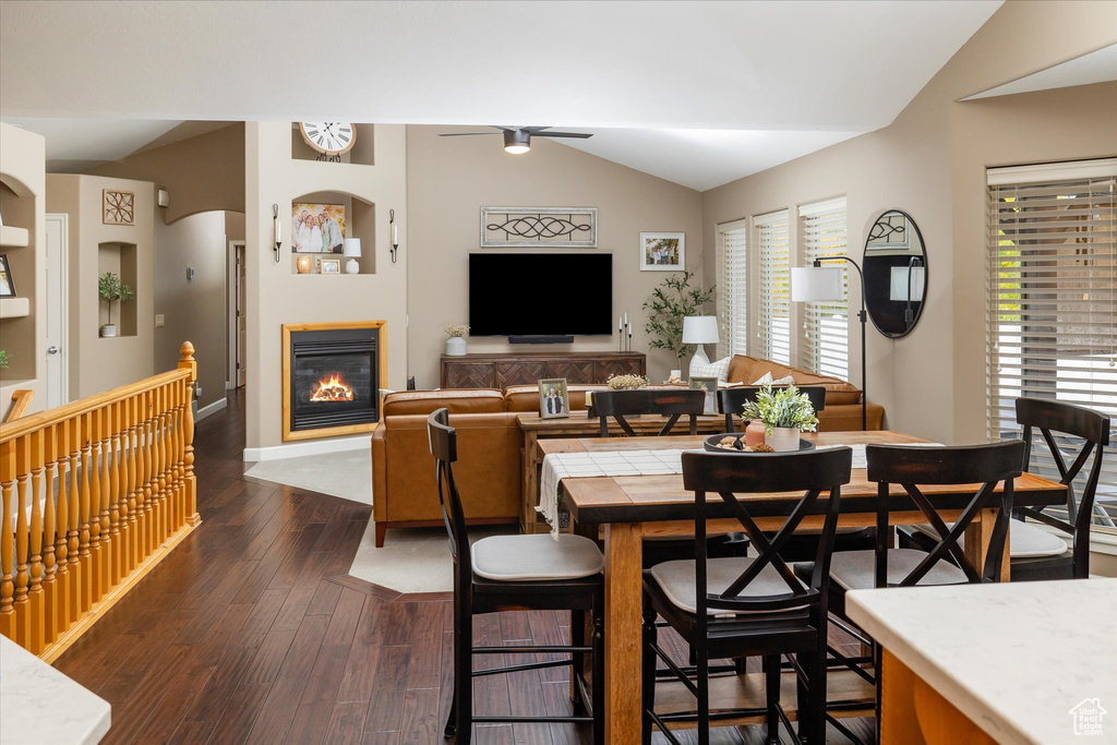 Dining area with vaulted ceiling, dark wood-style floors, a glass covered fireplace, ceiling fan, and baseboards