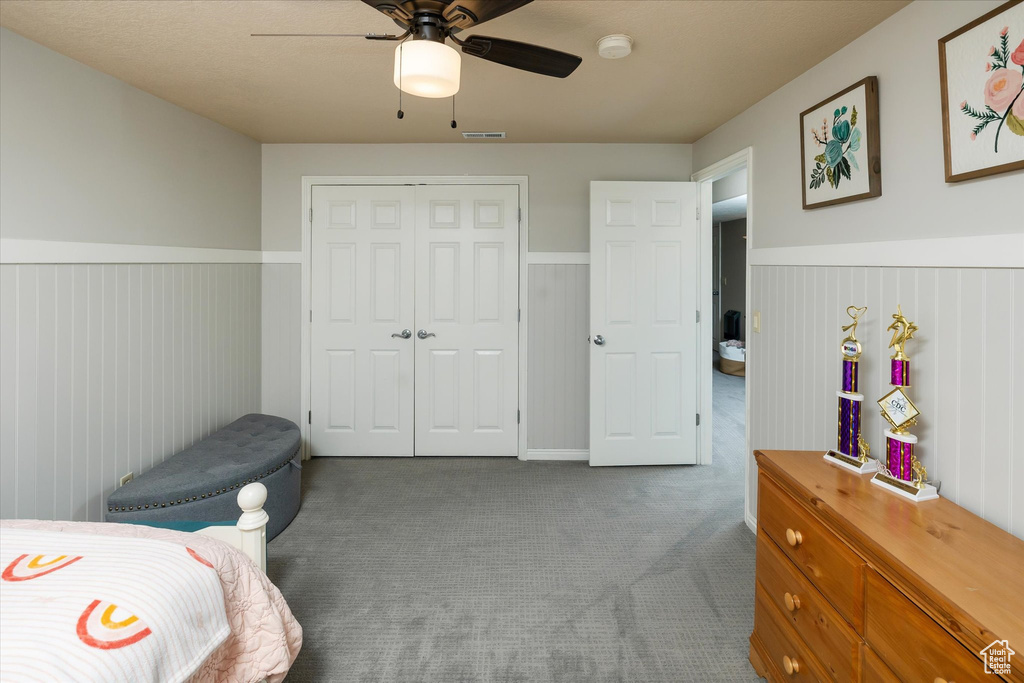 Carpeted bedroom with wainscoting, a closet, and a ceiling fan