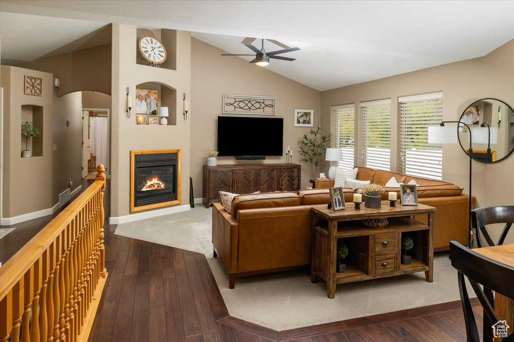 Living area featuring a ceiling fan, vaulted ceiling, a glass covered fireplace, dark wood finished floors, and baseboards