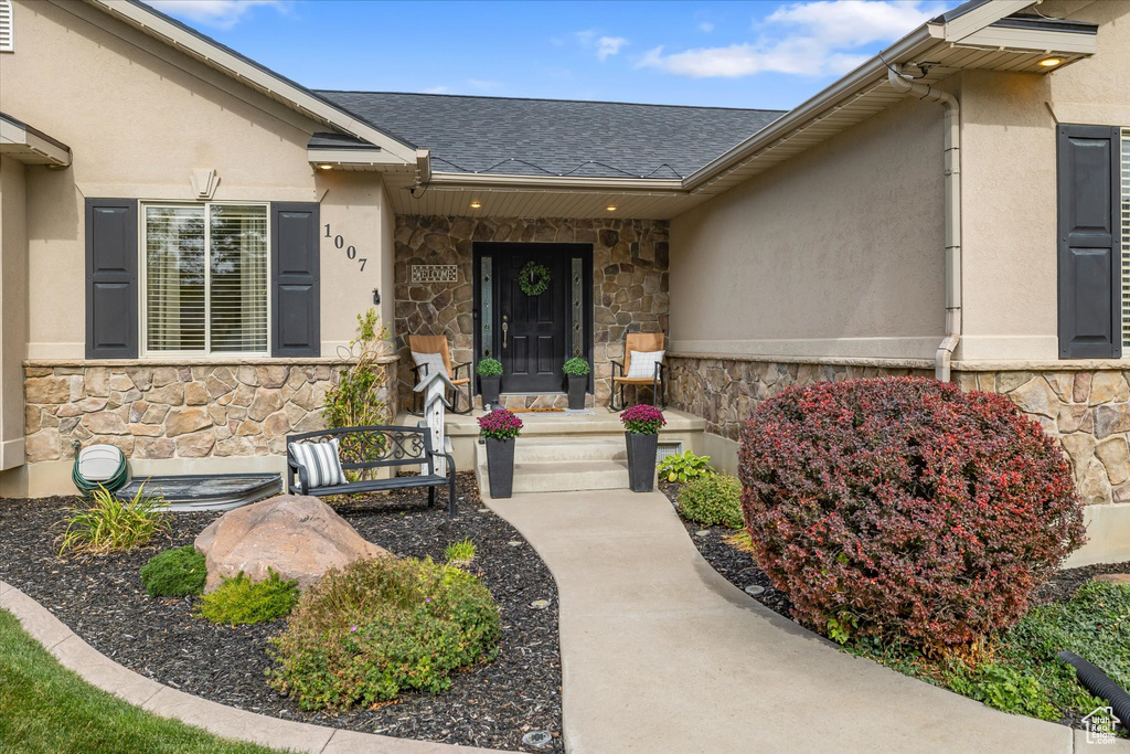 Entrance to property with stone siding, stucco siding, and a shingled roof