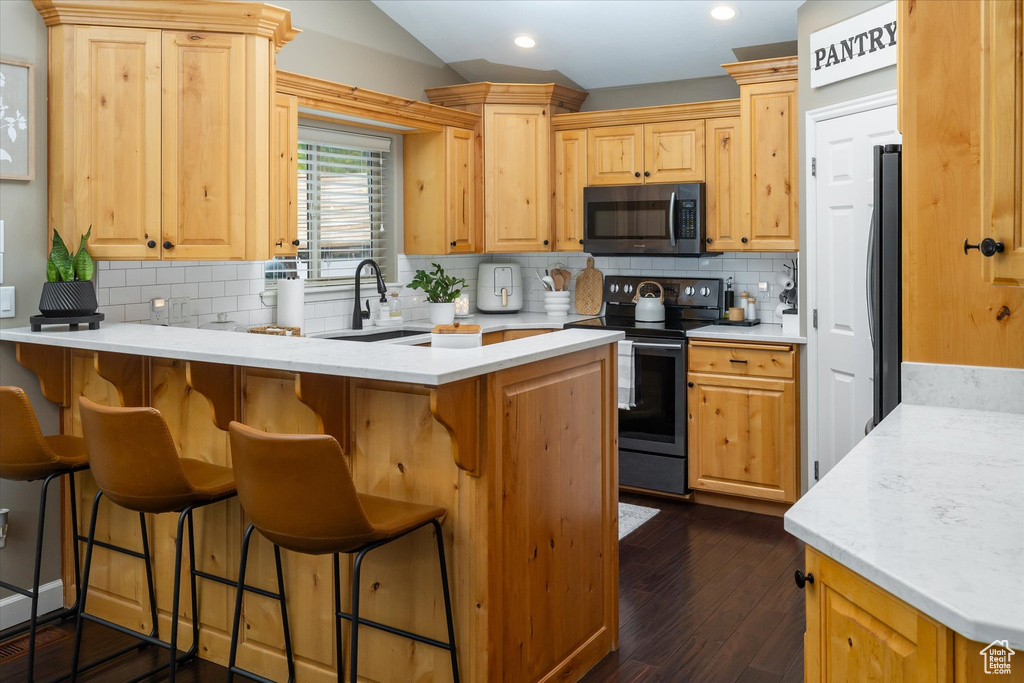 Kitchen featuring black electric range oven, stainless steel microwave, a peninsula, a sink, and tasteful backsplash
