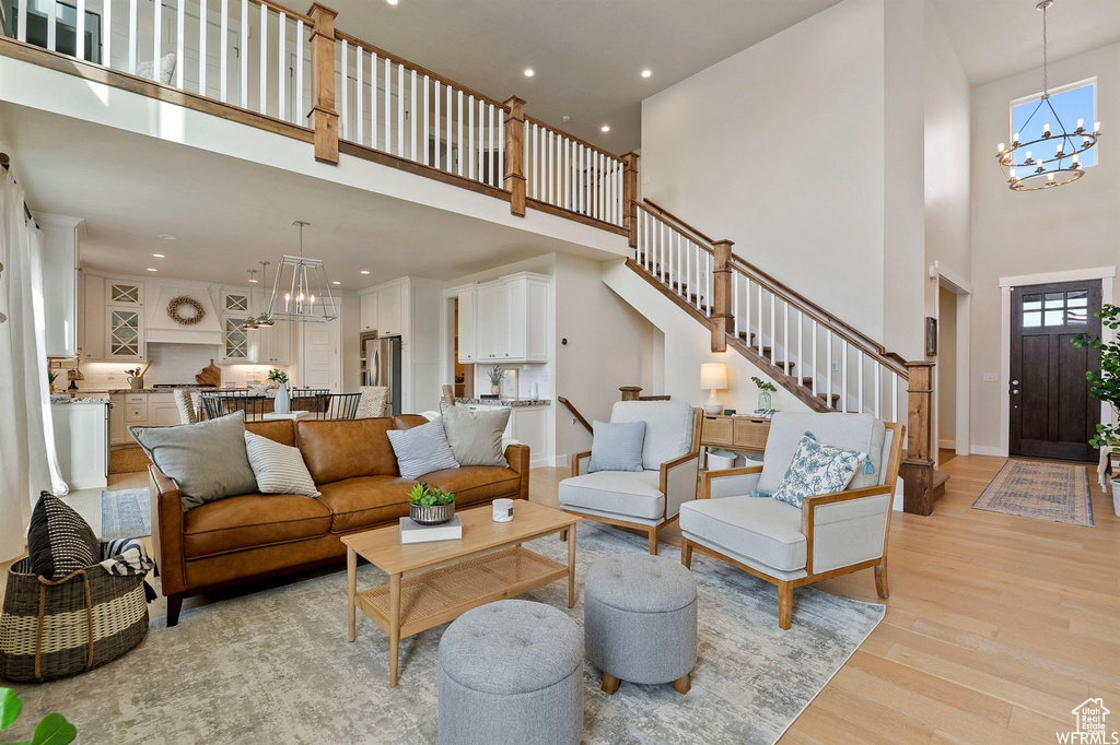 Living room with a chandelier, a high ceiling, light wood finished floors, stairway, and recessed lighting