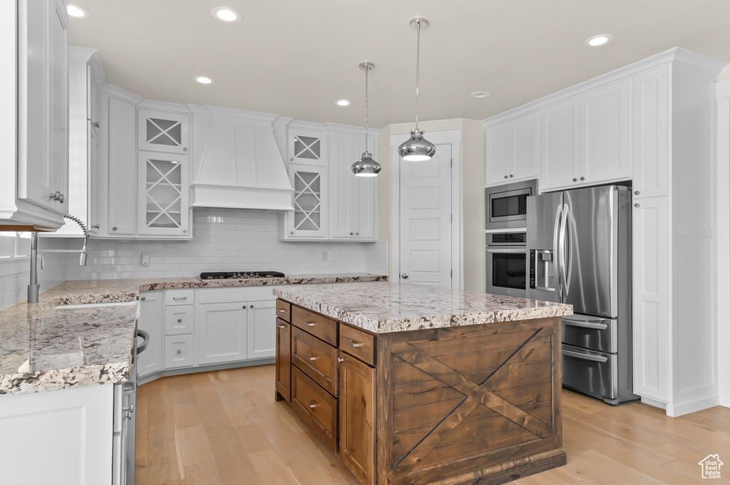 Kitchen with appliances with stainless steel finishes, custom range hood, a sink, light wood-style flooring, and white cabinetry