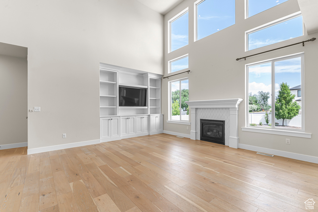 Unfurnished living room featuring a towering ceiling, light wood finished floors, baseboards, and a glass covered fireplace