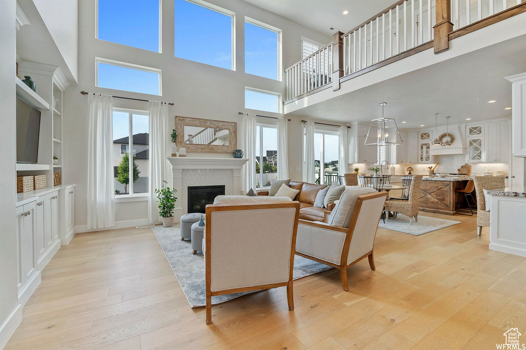 Living room featuring light wood-type flooring, a high ceiling, a glass covered fireplace, and recessed lighting