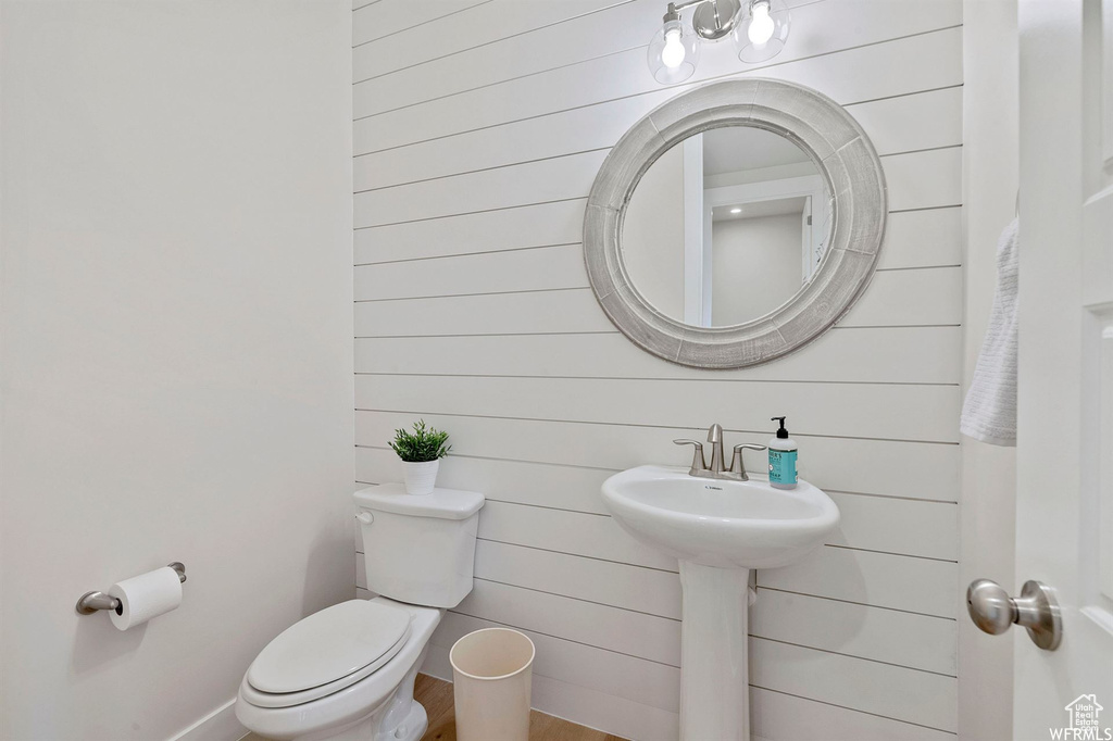 Half bathroom featuring toilet, wood finished floors, wooden walls, and baseboards