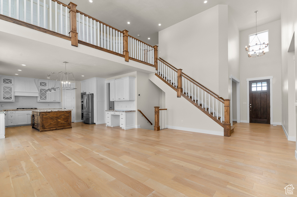Unfurnished living room featuring a towering ceiling, a chandelier, light wood-type flooring, recessed lighting, and baseboards