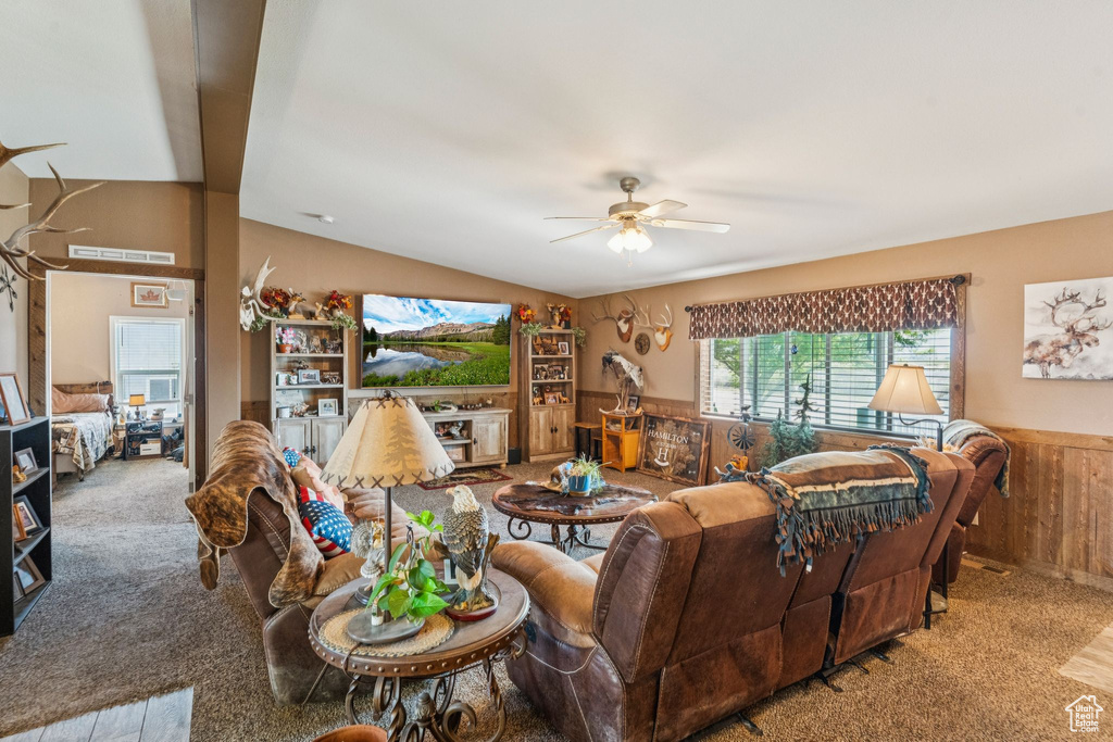 Living room with carpet, ceiling fan, a wainscoted wall, wood walls, and lofted ceiling
