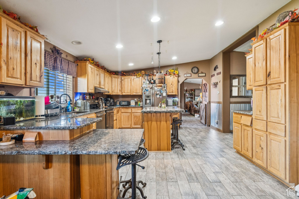 Kitchen featuring stainless steel appliances, a kitchen bar, a sink, dark stone countertops, and a peninsula