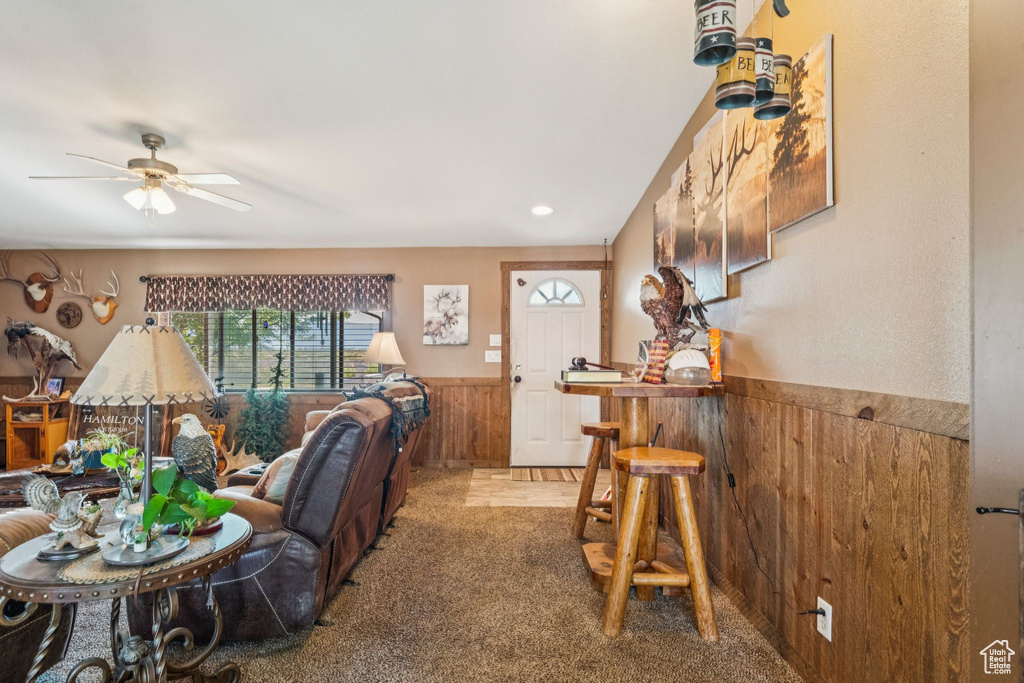 Living room featuring a wainscoted wall, wood walls, carpet, ceiling fan, and a dry bar