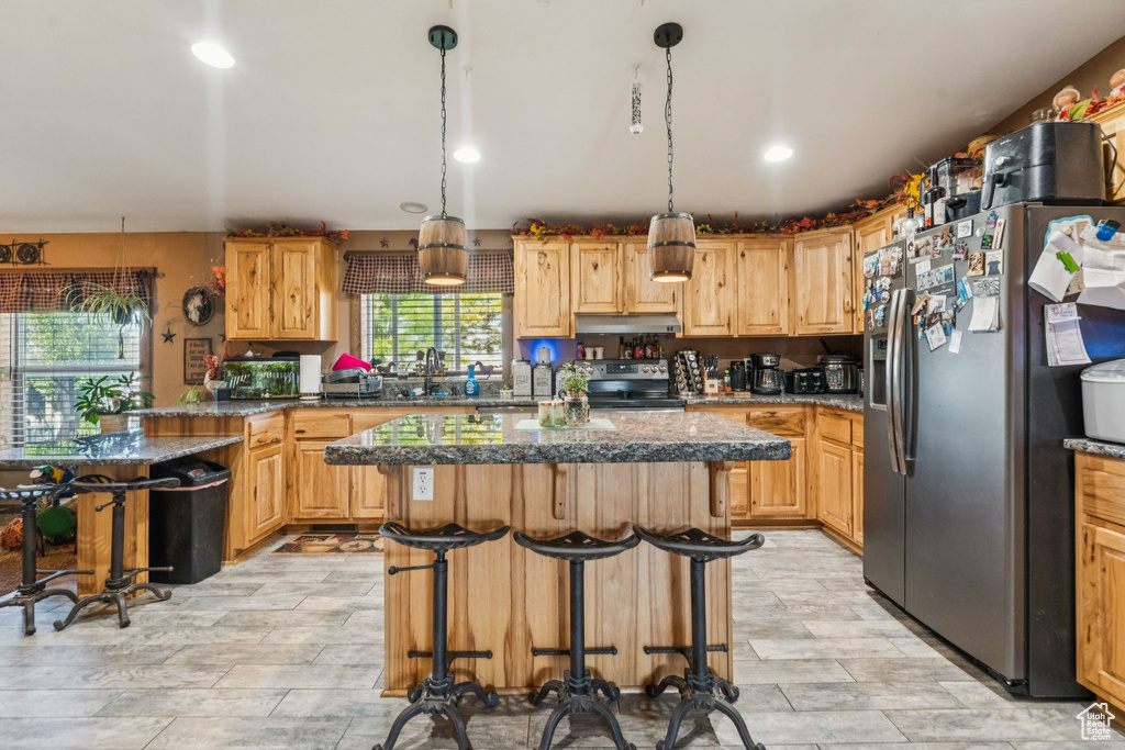 Kitchen featuring stainless steel fridge with ice dispenser, electric range oven, under cabinet range hood, a center island, and a kitchen breakfast bar