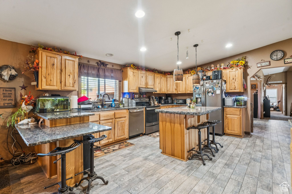 Kitchen with stainless steel appliances, a breakfast bar area, under cabinet range hood, light wood-type flooring, and recessed lighting