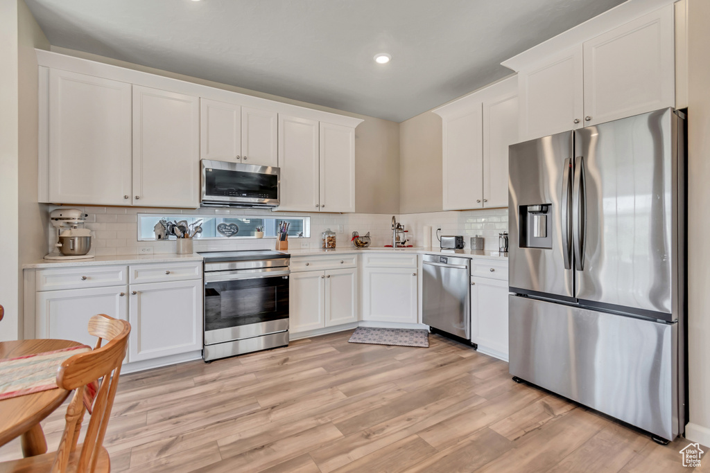 Kitchen featuring appliances with stainless steel finishes, white cabinetry, light countertops, decorative backsplash, and recessed lighting