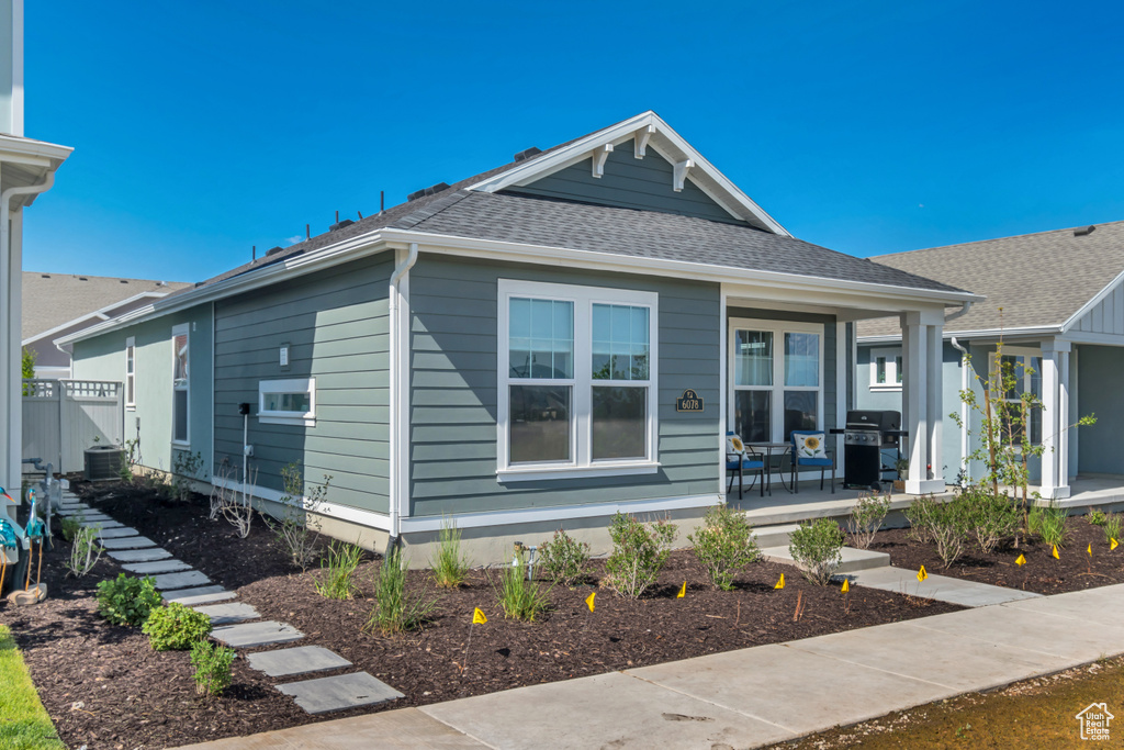 View of front of property with a porch, a shingled roof, and cooling unit