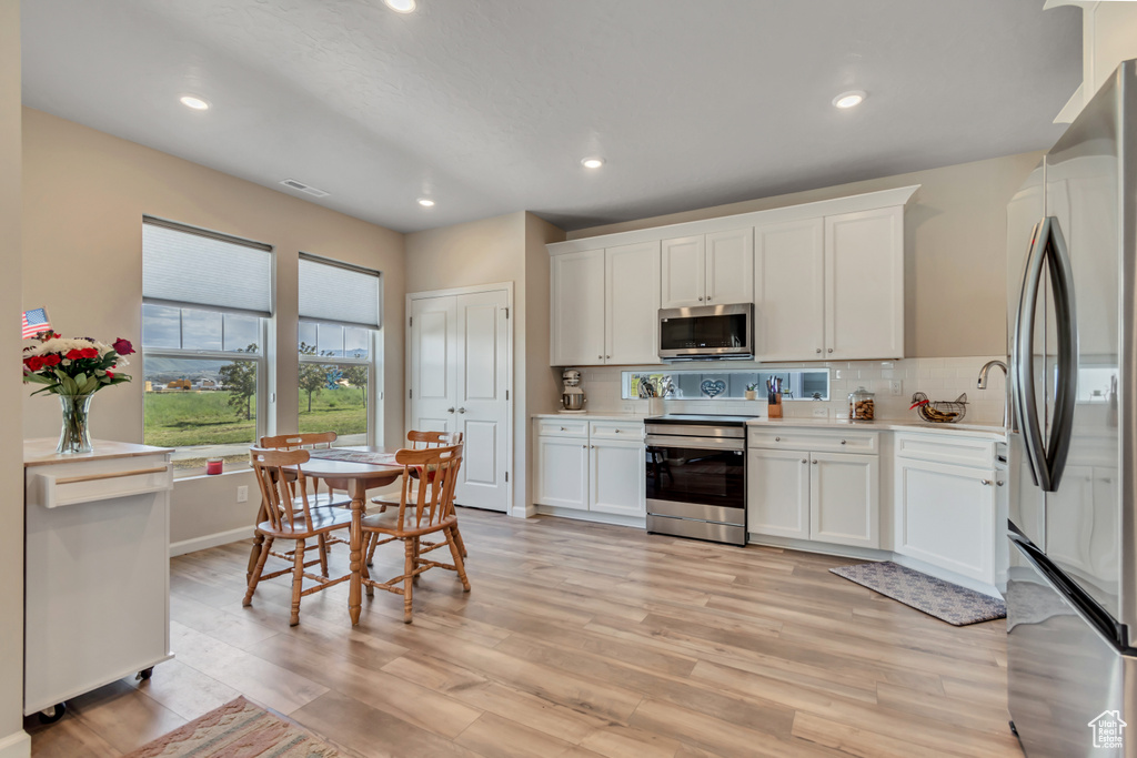 Kitchen featuring appliances with stainless steel finishes, light countertops, light wood-style flooring, decorative backsplash, and white cabinetry
