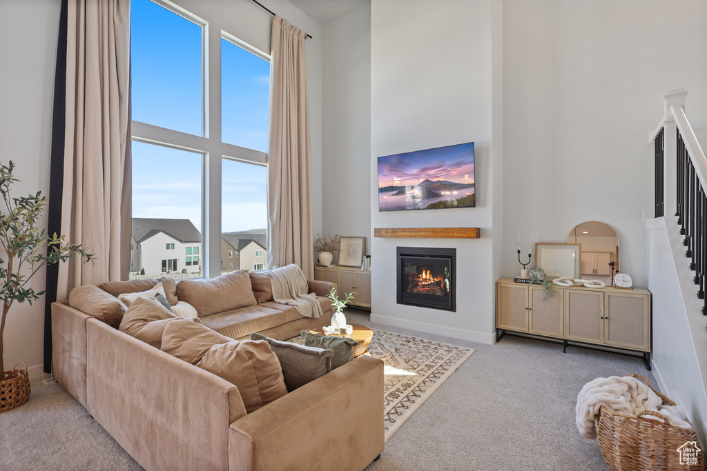 Living area featuring a towering ceiling, a glass covered fireplace, carpet flooring, baseboards, and stairway
