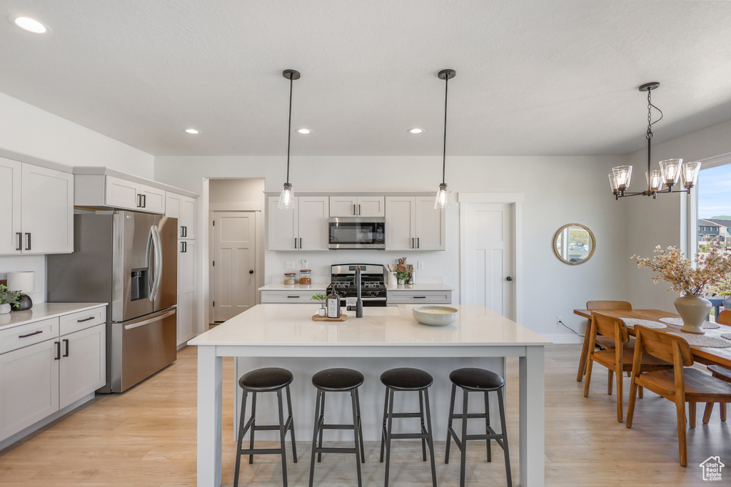 Kitchen with appliances with stainless steel finishes, light wood-style flooring, a chandelier, recessed lighting, and a breakfast bar