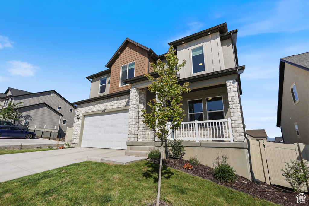 View of front of home with covered porch, stone siding, driveway, and a garage