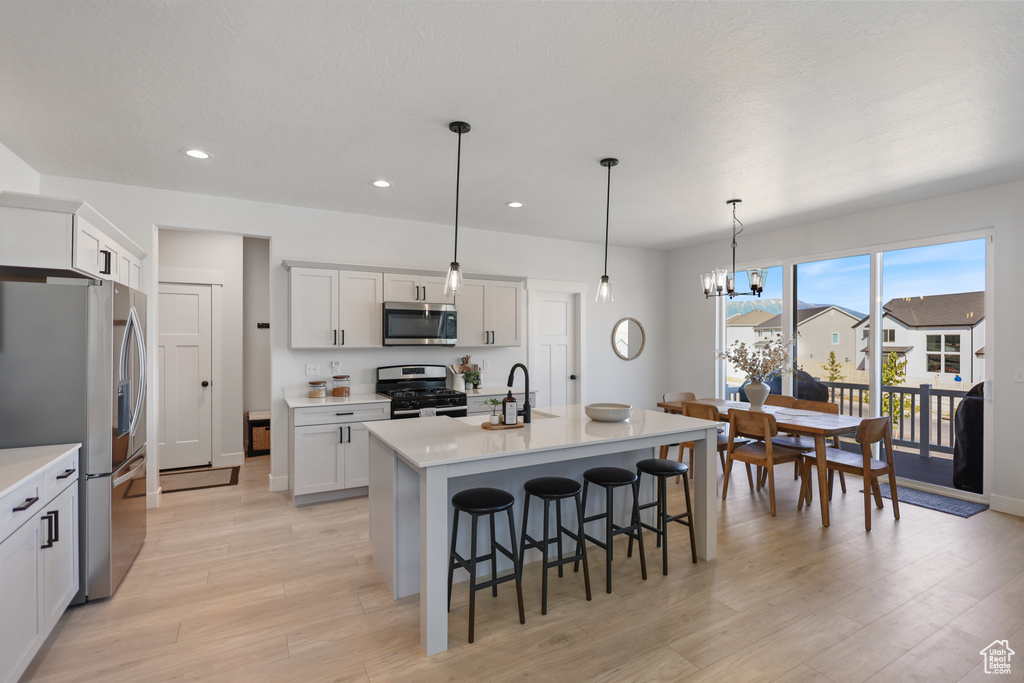 Kitchen with stainless steel appliances, light wood-style floors, a breakfast bar area, recessed lighting, and light countertops