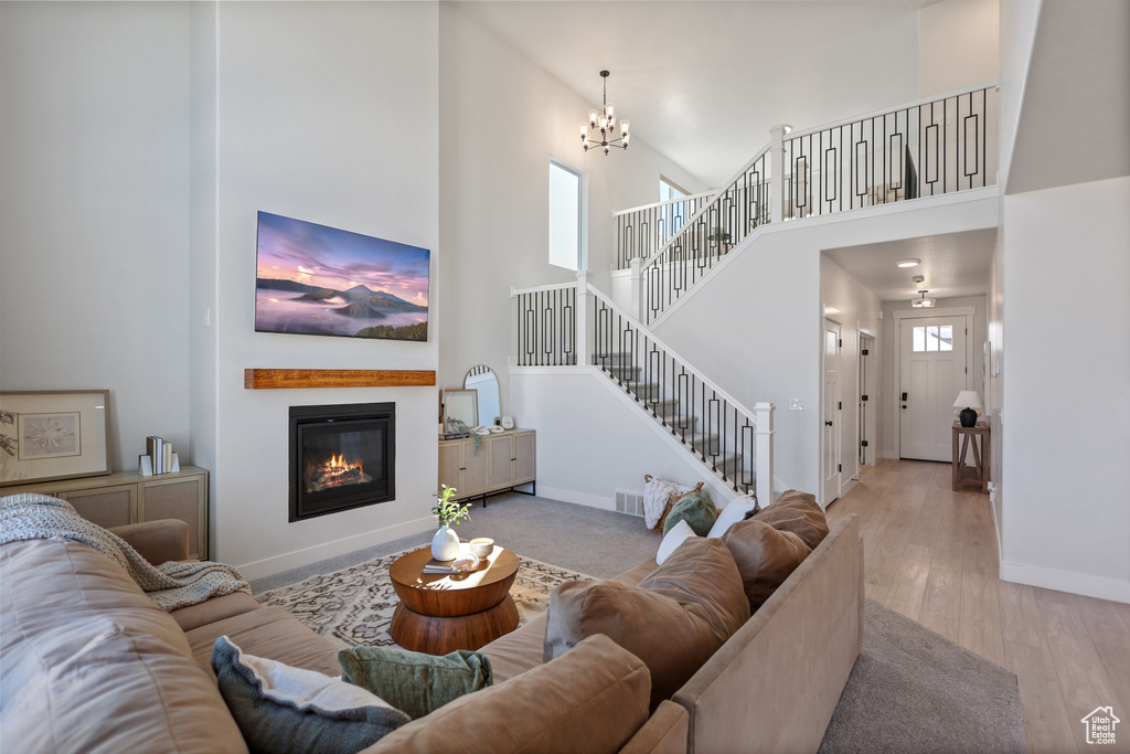 Living room with a high ceiling, stairs, baseboards, a chandelier, and a glass covered fireplace