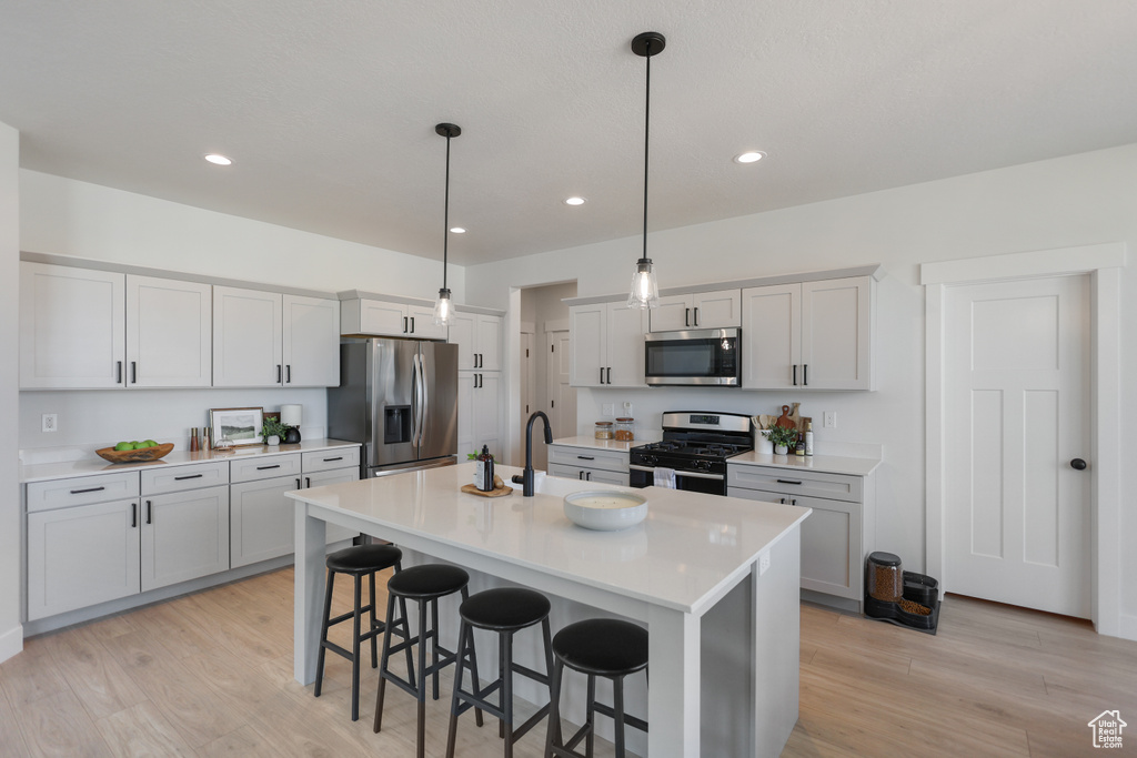 Kitchen featuring stainless steel appliances, a breakfast bar, a sink, a center island with sink, and light countertops