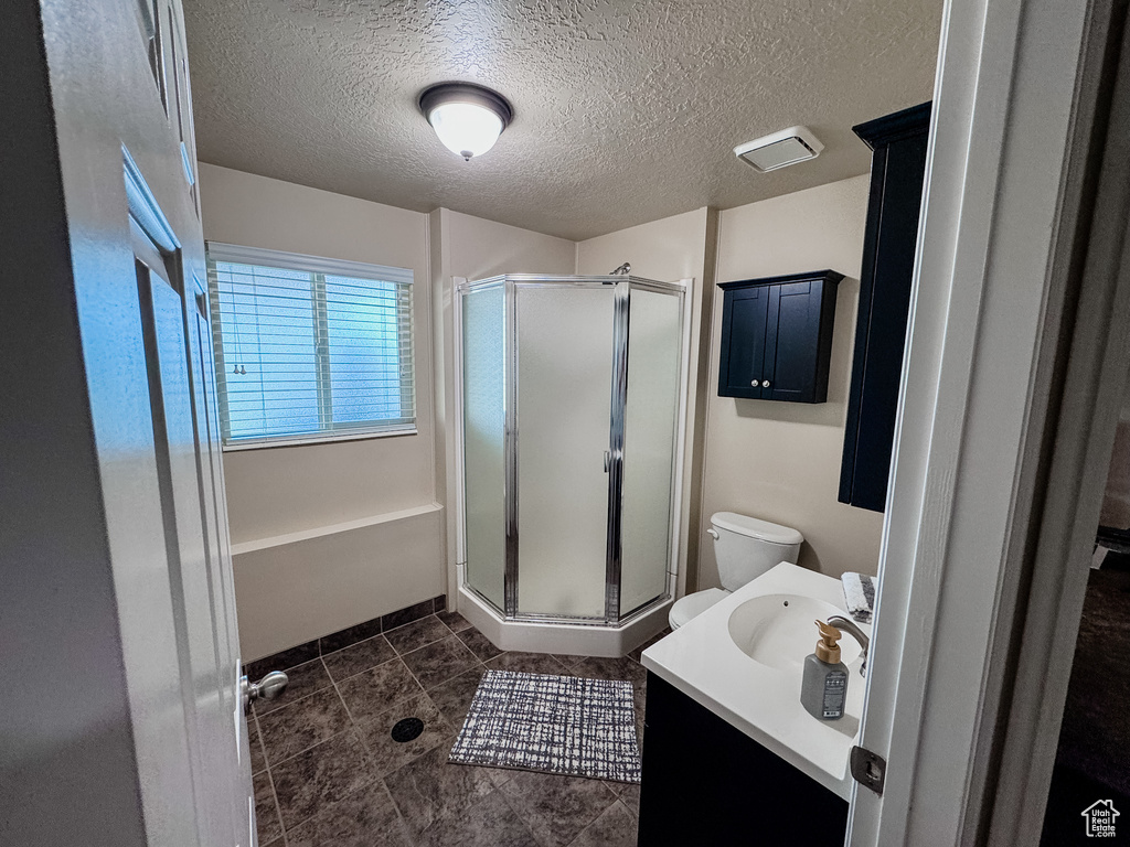 Bathroom featuring a shower stall, vanity, a textured ceiling, toilet, and tile patterned floors