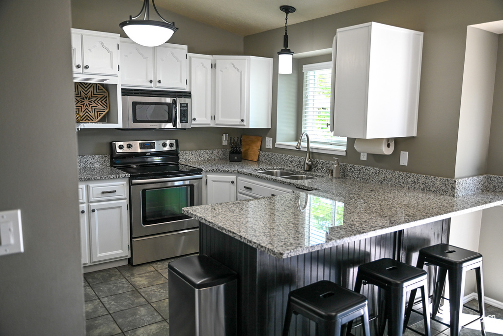 Kitchen featuring stainless steel appliances, a peninsula, a sink, white cabinetry, and a breakfast bar area