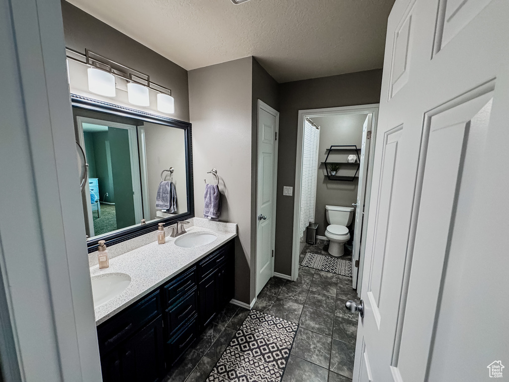 Bathroom featuring double vanity, toilet, a textured ceiling, and baseboards