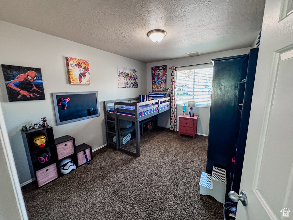 Bedroom with dark carpet, a textured ceiling, and baseboards