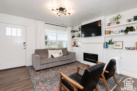 Living room featuring dark wood-style flooring, a chandelier, a glass covered fireplace, and built in shelves