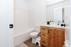 Full bath with vanity, toilet, wood finished floors, and  shower combination