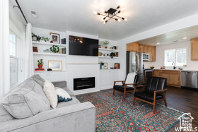 Living area with a chandelier, healthy amount of natural light, a glass covered fireplace, and dark wood-style flooring