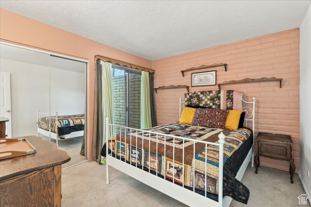 Carpeted bedroom with a closet, brick wall, and a textured ceiling