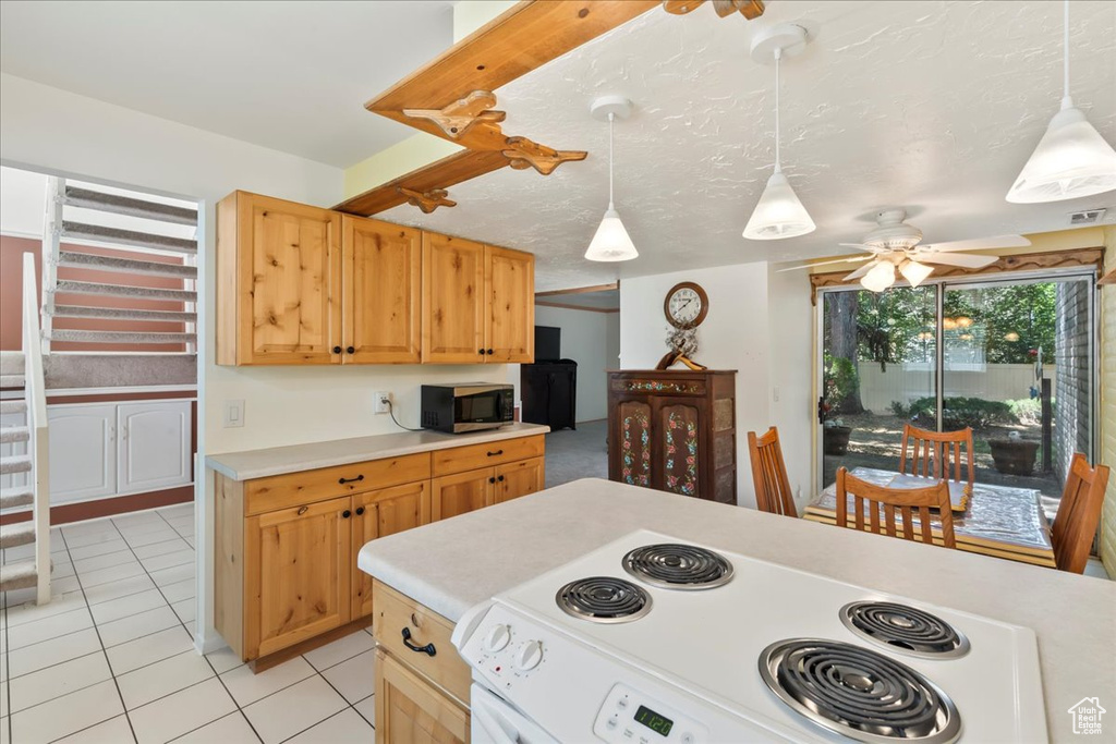Kitchen featuring stainless steel microwave, stove, light countertops, a ceiling fan, and light tile patterned floors
