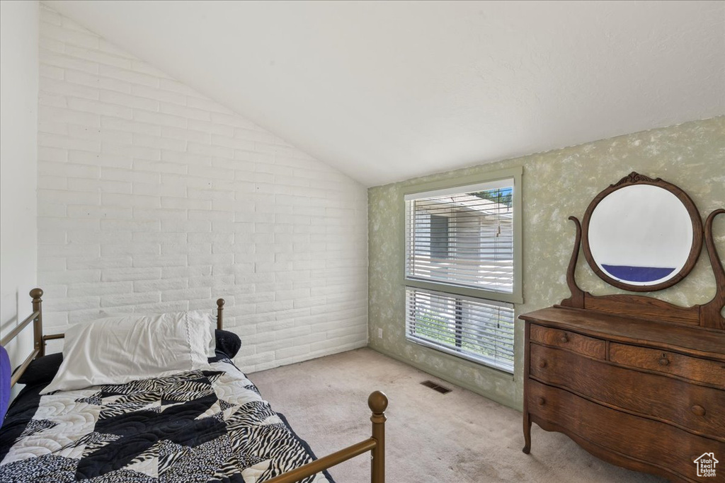 Carpeted bedroom with lofted ceiling and brick wall