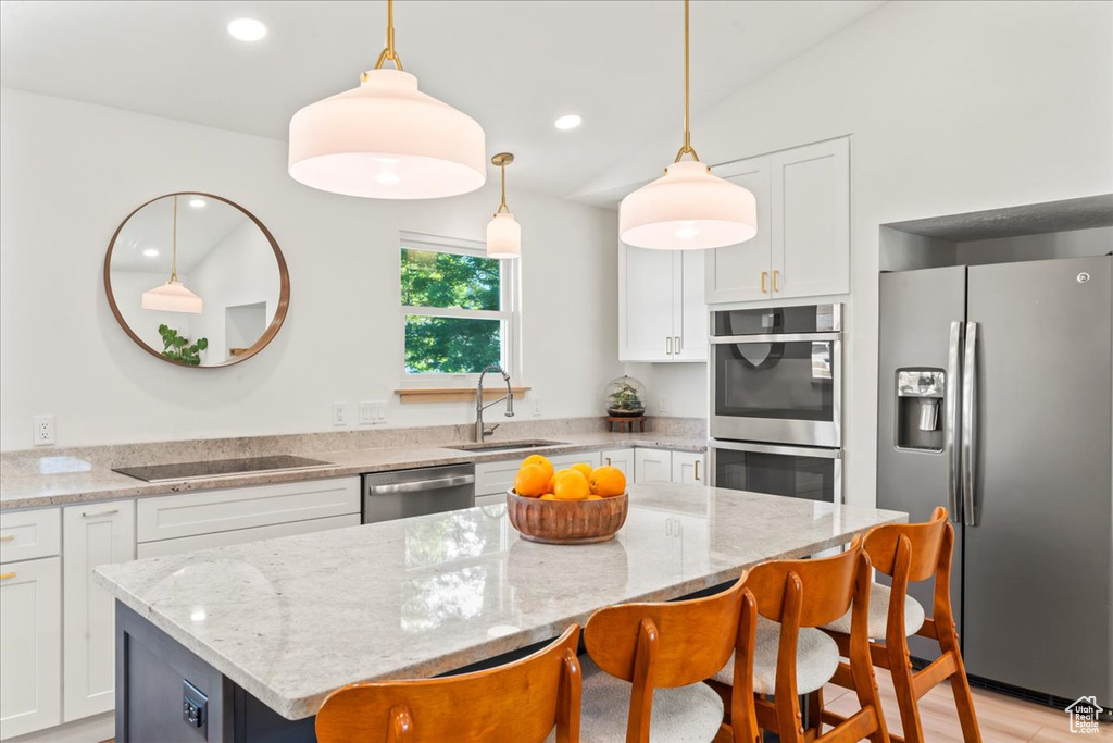 Kitchen with appliances with stainless steel finishes, a sink, a kitchen breakfast bar, a center island, and white cabinetry